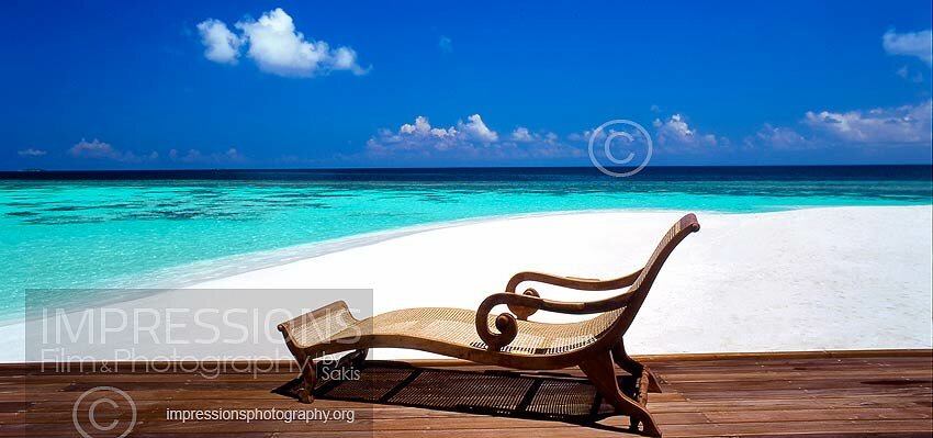 sun lounger on wooden deck with view at tropical beach and lagoon
