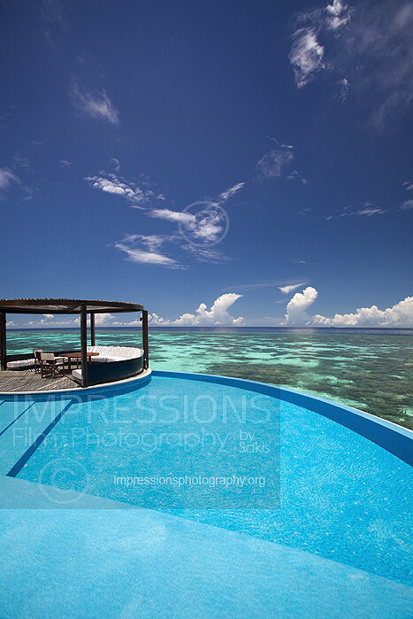 Maldives, deck of a water villa at Maldives resort with luxury sofa infinity swimming pool and lagoon with coral reefs and ocean view stock photo