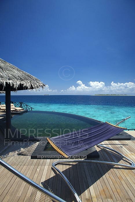 Maldives, wooden Deck of a water villa at resort with hammock and infinity pool with ocean view stock photo