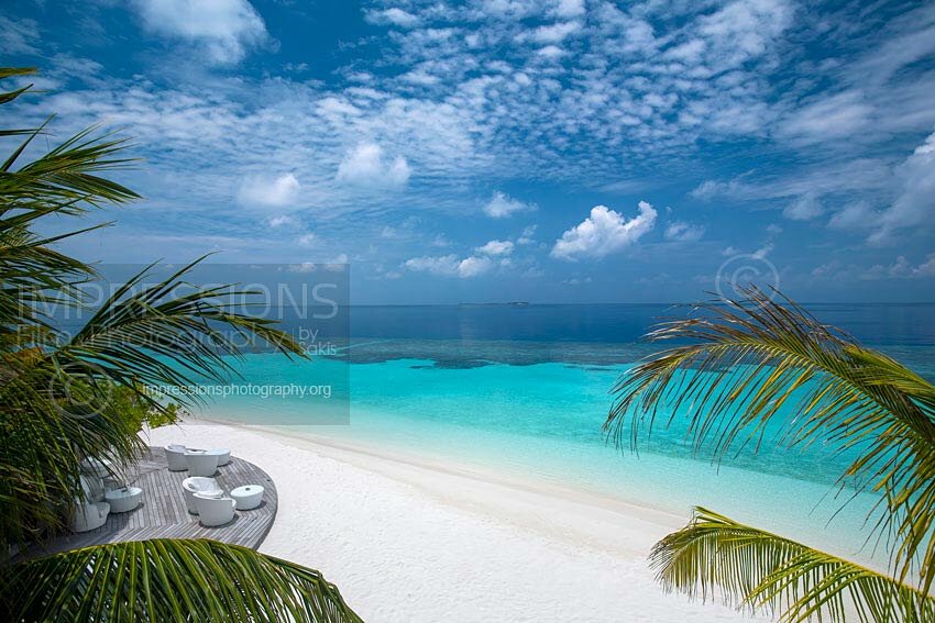 Maldives chairs on wooden deck with a beautiful beach and coconut palm trees looking at blue lagoon stock photo