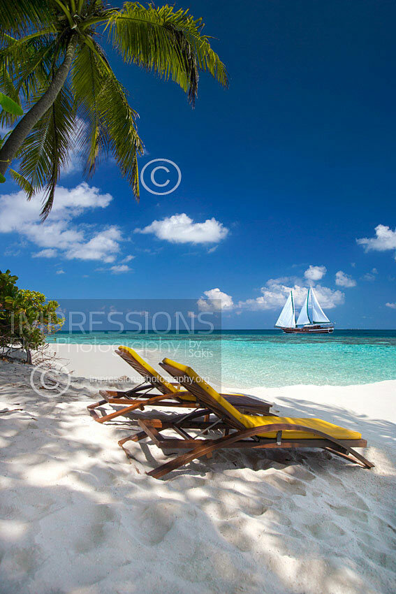 Maldives lounge chairs on tropical beach and sailing boat stock photo