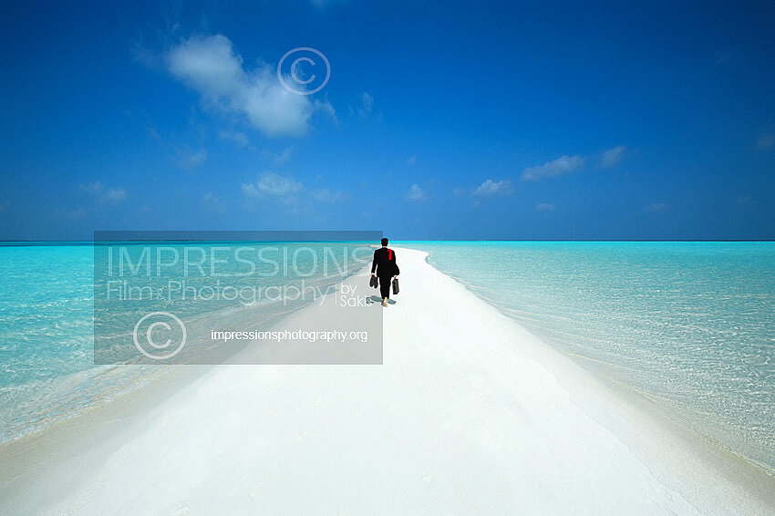 Business man wearing suit walking along sandbank in Maldives