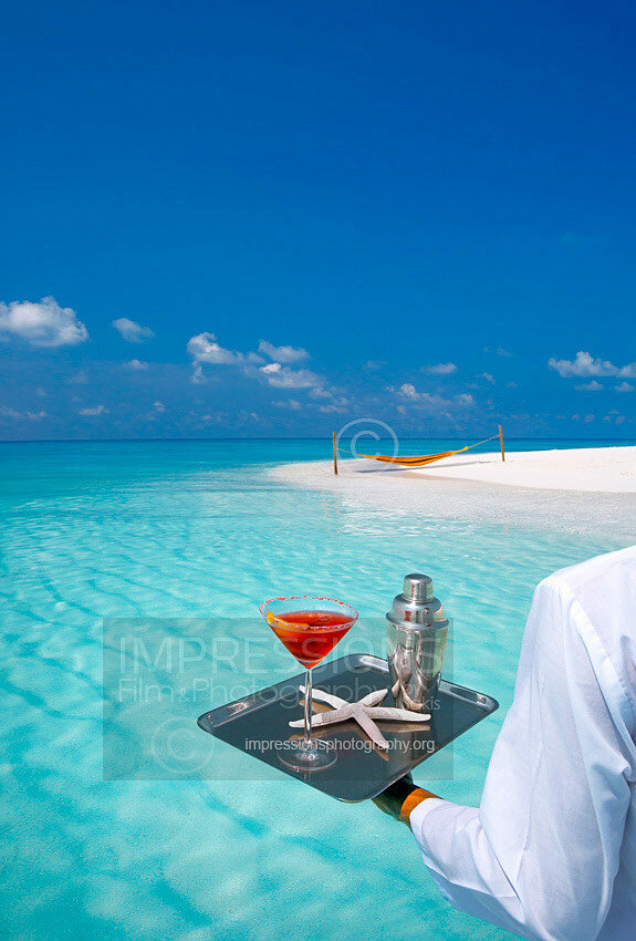 Waiter carrying cocktail on tropical beach with a hammock and sandbank Maldives stock photo