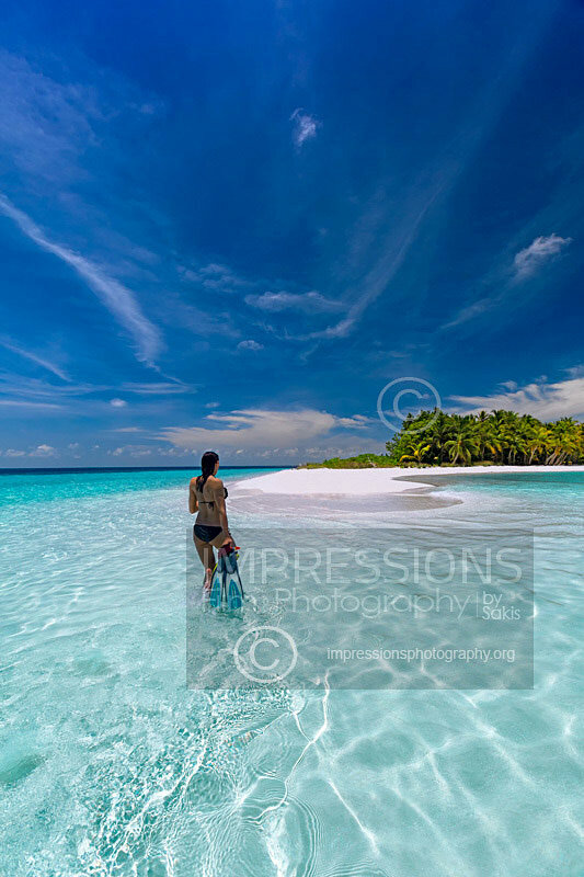 woman with snorkelling gear walking in blue lagoon on tropical beach looking at a tropical island Maldives stock photo