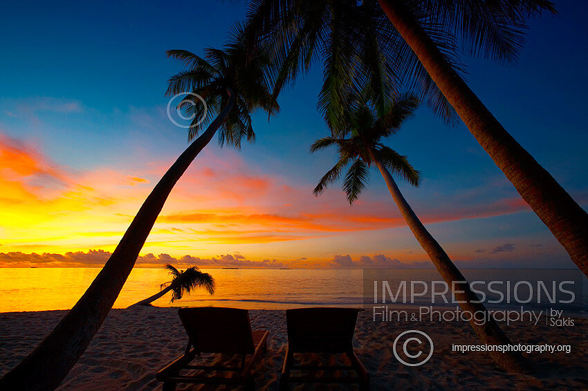Maldives sunset with Lounge Chairs on tropical beach and coconut palm trees stock photo