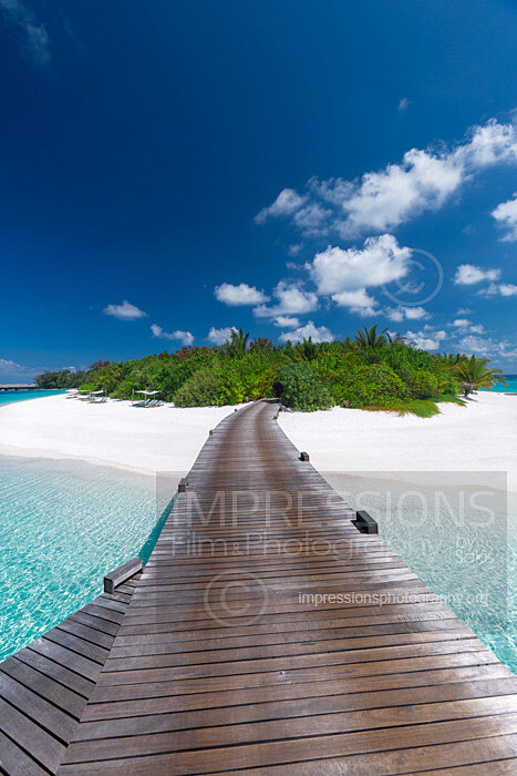 Maldives stock photo of a wooden jetty leading to a tropical island over blue lagoon