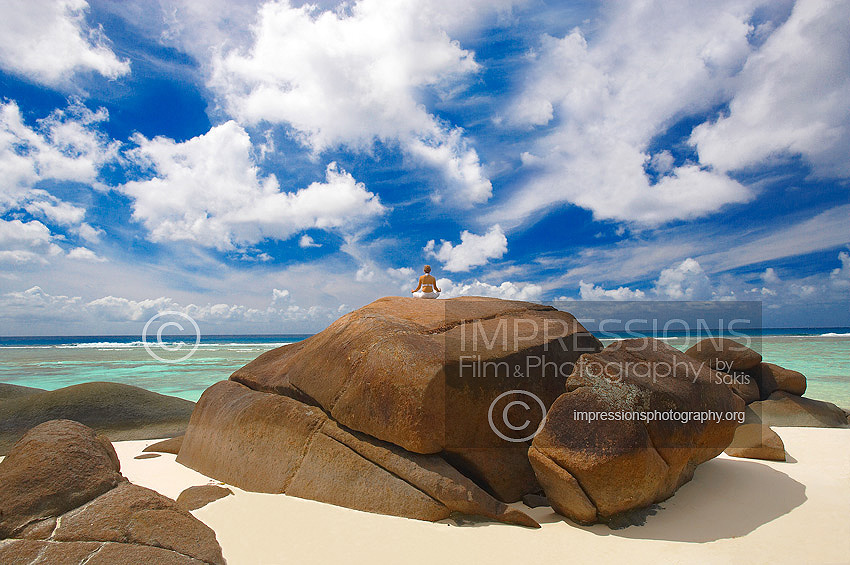 Young woman meditating on rock at the beach, Seychelles